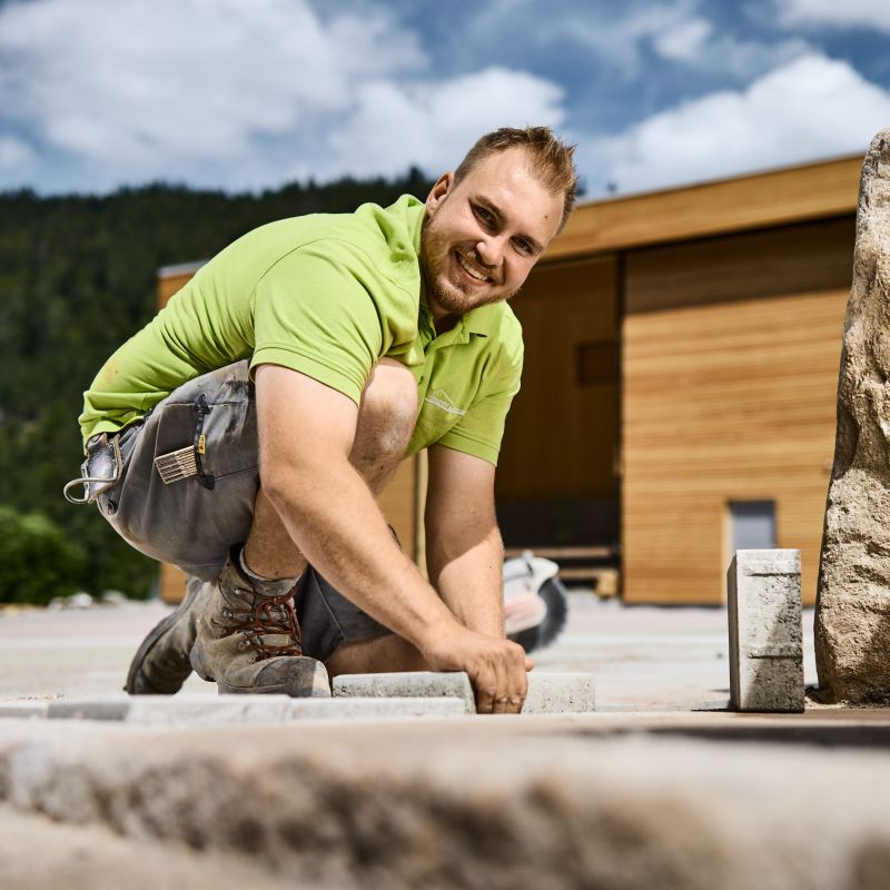 Mitarbeiter GianLuca Martino auf einer Baustelle mit Pflastersteinen in den Händen